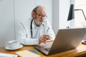 male doctor at desk laptop computer thinking